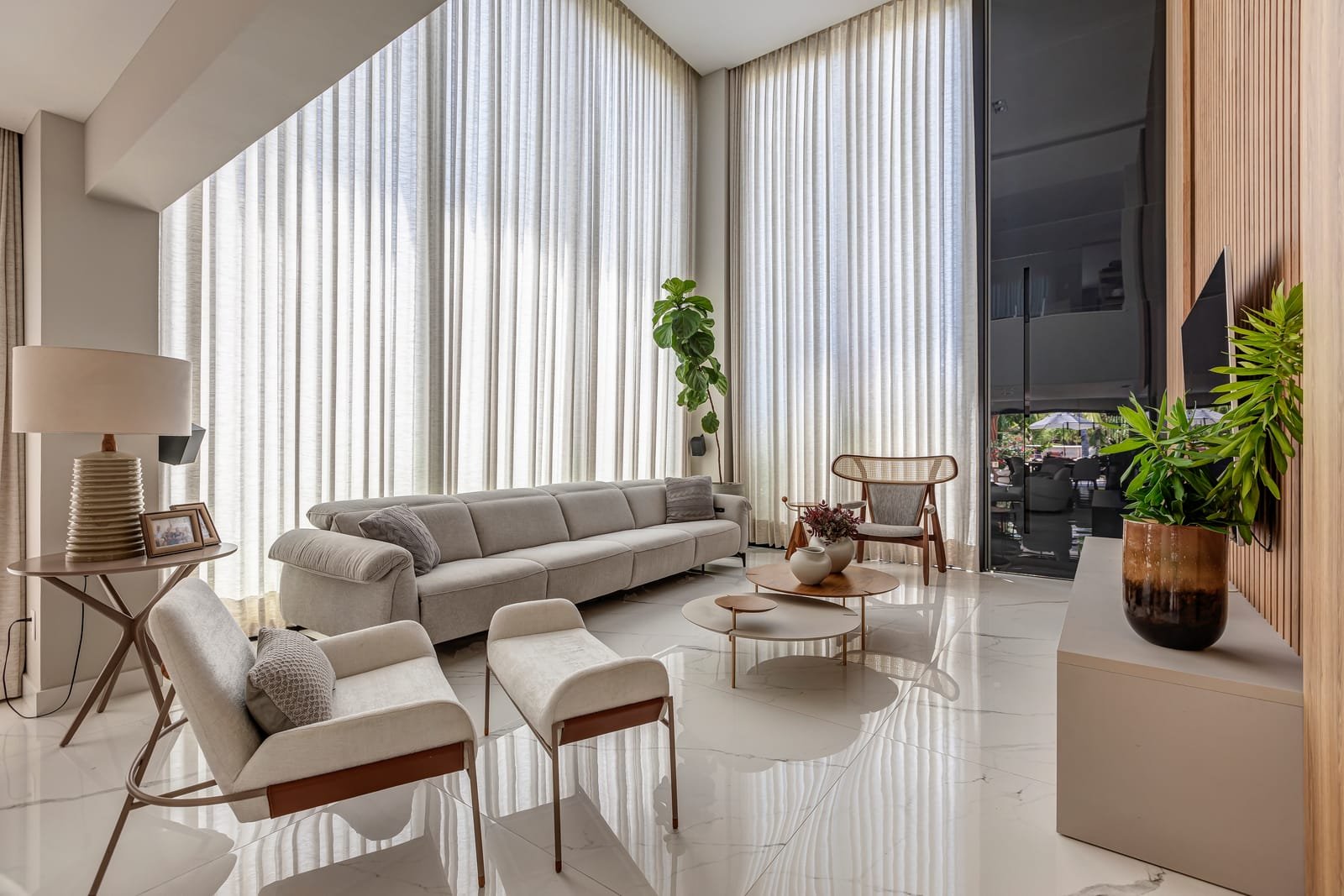 Estar de pé-direito duplo com cortinas do chão ao teto, sofá claro e piso de mármore.